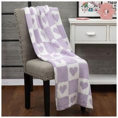 a chair with a purple and white blanket on top of it next to a dresser