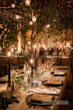 a table set for dinner with candles and greenery in the center, surrounded by glass vases