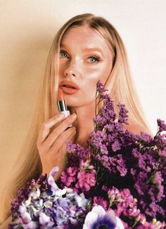 a woman with long blonde hair holding a lipstick in front of her face