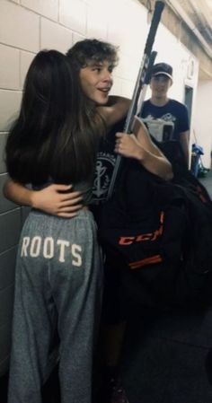 two young people standing in a hallway with baseball equipment on the wall and one person holding a bat