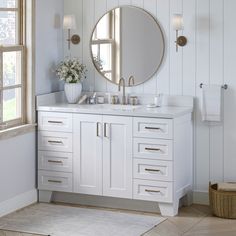 a white bathroom with two sinks and a round mirror on the wall next to a window