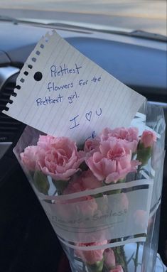 pink carnations in a vase with note attached to the back of a car