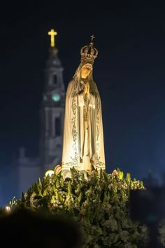 a golden statue with a crown on top in front of a tall building at night