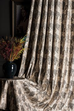 a vase filled with flowers sitting on top of a table next to a window curtain