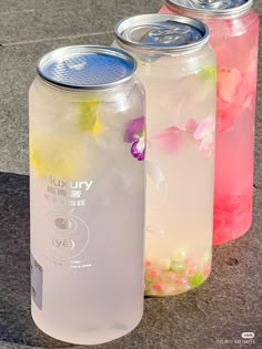 three soda cans with flowers in them sitting on the ground next to each other,