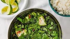 a pan filled with green vegetables next to rice and lime wedges on a table