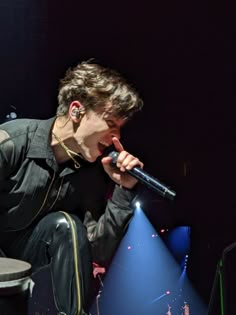 a male in a black shirt is on stage with a microphone and lights behind him