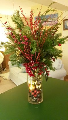 a vase filled with red berries and greenery sitting on top of a green table