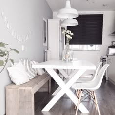 a white dining table and bench in a room with wood flooring on the side