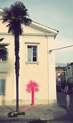 a palm tree is painted on the side of a building with a pink ribbon tied to it