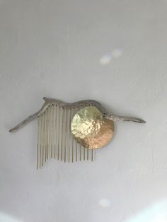 a metal comb hanging from the ceiling next to a tree branch with a gold disc on it