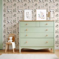 a green dresser sitting in front of a wallpapered wall with animals on it