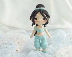 a crocheted doll is standing on a white sheet with colorful lights in the background