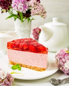 a piece of strawberry cheesecake on a plate with flowers and teapots in the background