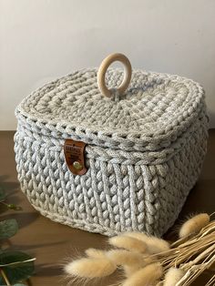 a white knitted basket sitting on top of a wooden table next to dried plants