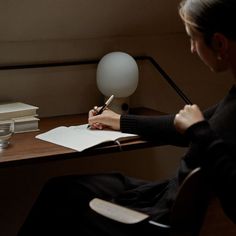 a woman sitting at a desk writing on a piece of paper with a pen in her hand