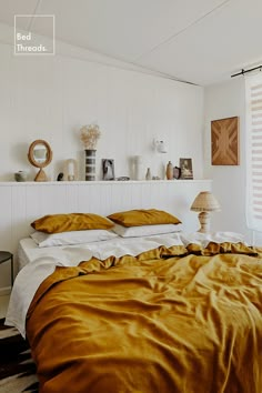 a bed with gold sheets and pillows in a white room next to a wall mounted shelf