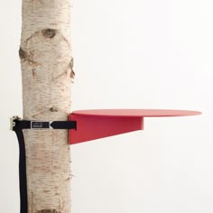 a red table sitting on top of a tree next to a white wall with a black strap around it