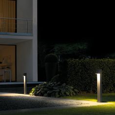 two lights that are in the grass near a house at night with one light on