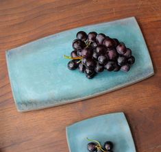 two blue plates with grapes on them sitting on a wooden table next to each other