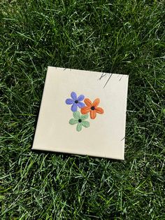 a piece of paper with flowers painted on it laying in the grass next to some scissors