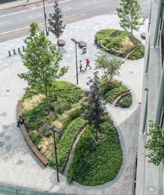 an aerial view of people walking on the sidewalk in front of some trees and bushes