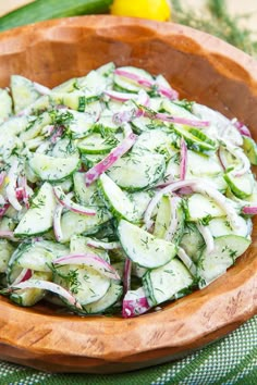 a wooden bowl filled with cucumbers, onions and fennel on top of a table