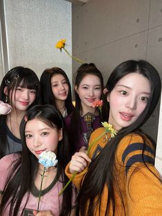 a group of young women standing next to each other holding flowers in their mouths and smiling at the camera