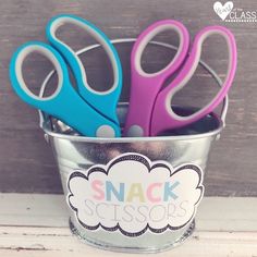 three colorful scissors are in a metal cup on the table next to a sign that says snack scissors