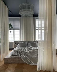 a large bed sitting under a chandelier in a bedroom next to two windows