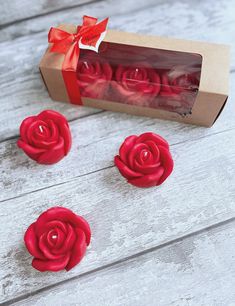 three red roses sitting in front of a box on a wooden table next to some candles