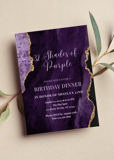 an elegant purple and gold birthday party card on a table with greenery next to it