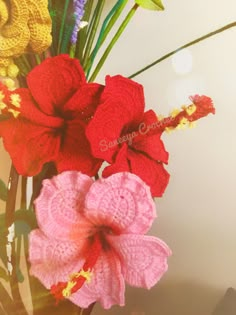 two crocheted flowers in a vase with green leaves and purple, red, yellow and pink flowers