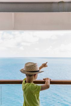 a young boy wearing a straw hat looking out at the ocean from a cruise ship