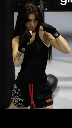 a woman with long hair wearing black boxing gloves and holding her fist in one hand