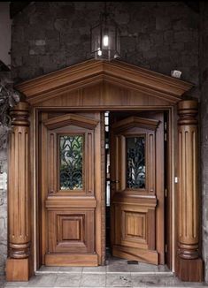 two wooden doors are open in front of a stone wall and planters on either side