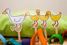 three ducks and two geese on wooden sticks in front of a green pillow with toys