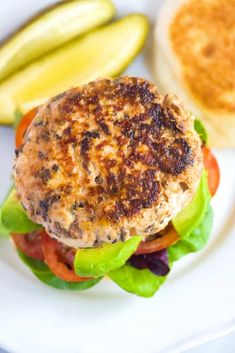 a burger with lettuce, tomato and pickles on a white platter