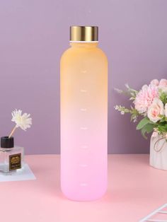 a pink and yellow bottle sitting on top of a table next to a vase with flowers