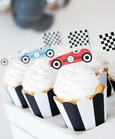 cupcakes with white frosting and race cars on them are sitting in black and white striped paper cups