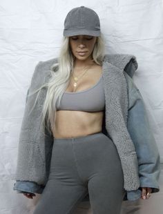 a woman with long hair wearing grey pants and a gray hat is standing in front of a white backdrop