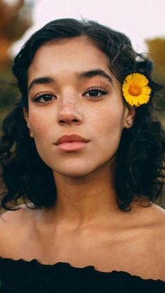 a woman with a yellow flower in her hair looking off to the side while wearing a black top