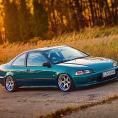 a green car parked on the side of a road next to tall grass and trees