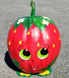 a painted pumpkin sitting on the ground with eyes and nose drawn to look like a strawberry