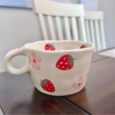 a white cup with strawberries on it sitting on a table next to a chair