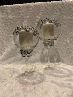 two clear glass candlesticks sitting on top of a white cloth covered tablecloth