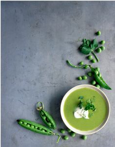 a bowl filled with green pea soup next to peas and sprouts on a table