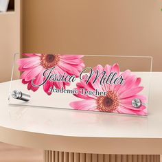 an acrylic sign with pink flowers on it sitting on top of a table