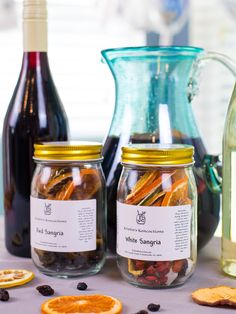 three jars filled with different types of food next to bottles of wine and orange slices