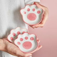 two hands holding pink and white dishes with paw prints